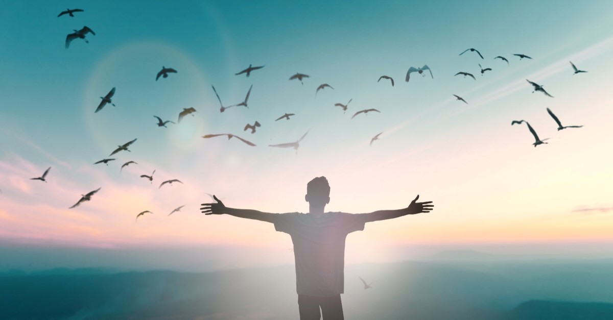 happy man standing on cliff with hands raised, god's presence manifest presence vs omnipresence