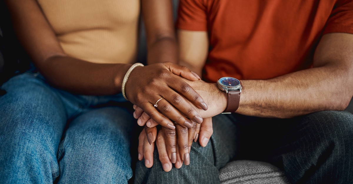 married couple holding hands praying on couch