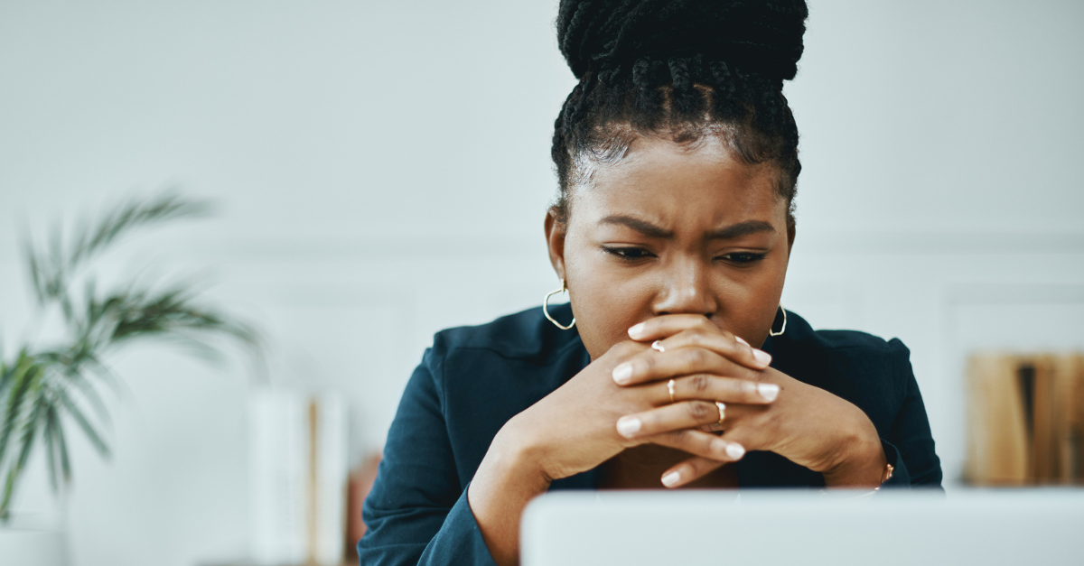 Frustrated woman staring at computer with her hands clasped over her mouth.