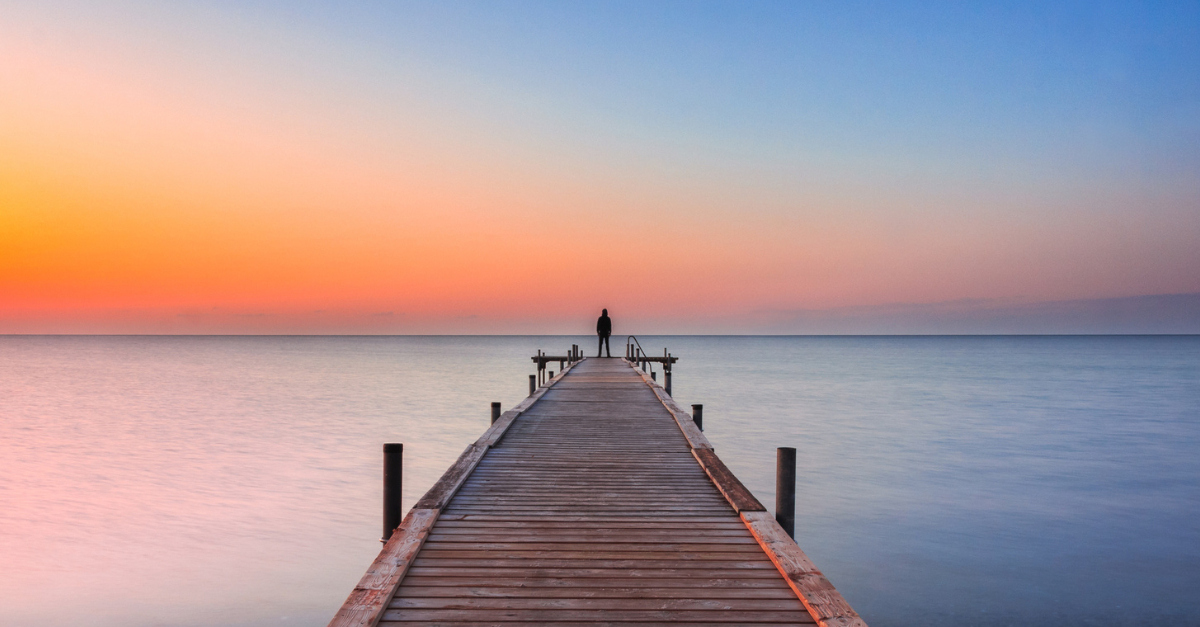 Person watching the sunrise at the end of a long dock over the water.