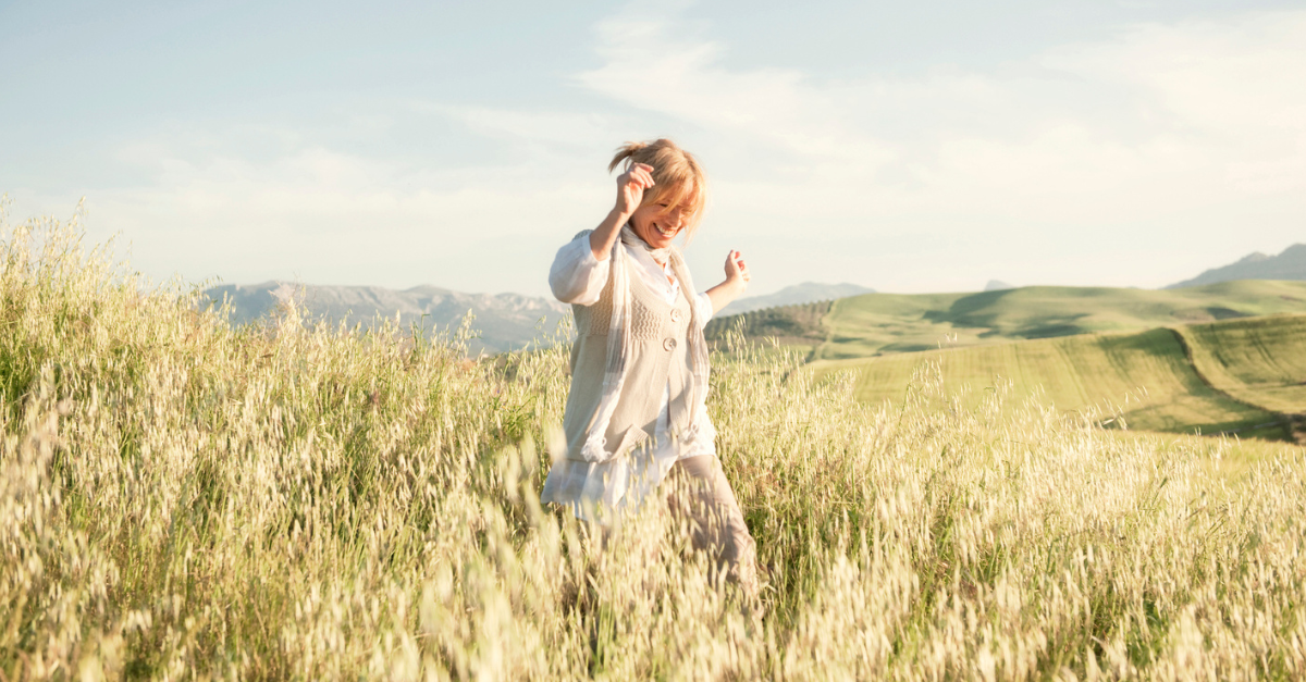 Woman singing joyfully as she walks through a field on a sunny day.