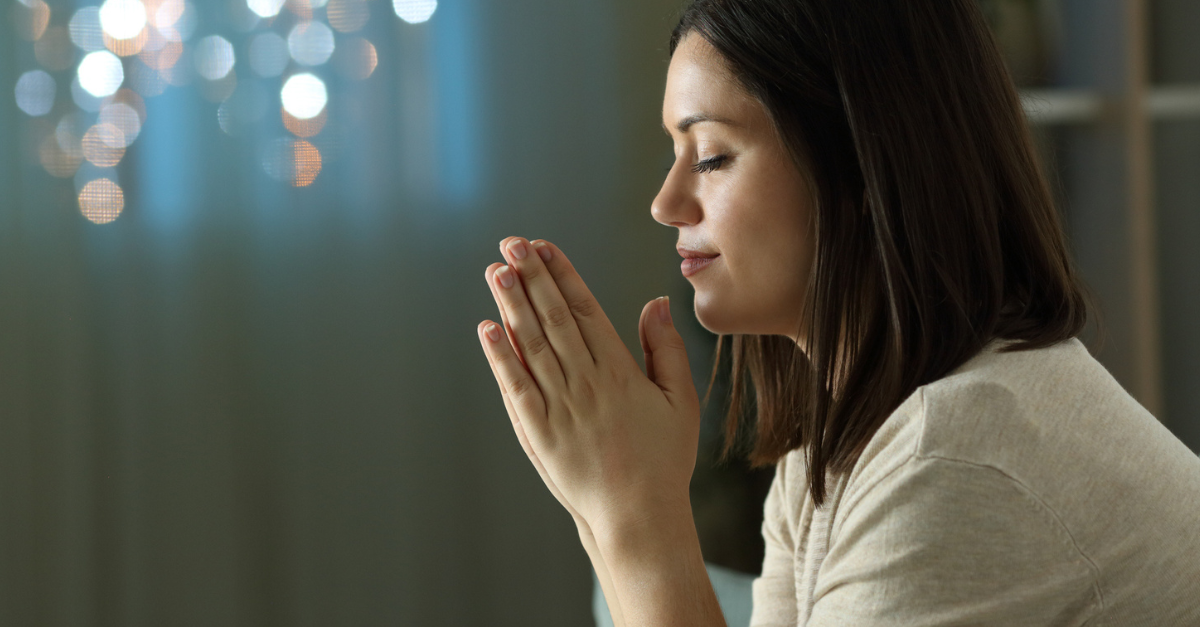 Woman kneeling at her bedside, eyes closed, praying; a midnight prayer of intercession.