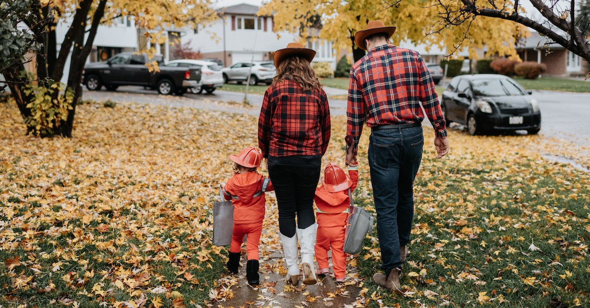 mom and dad holding little kids hands trick or treating on halloween