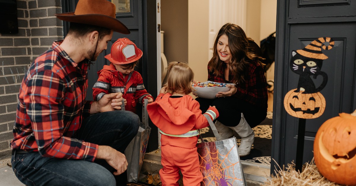 woman smiling at trick or treating family on halloween handing out candy