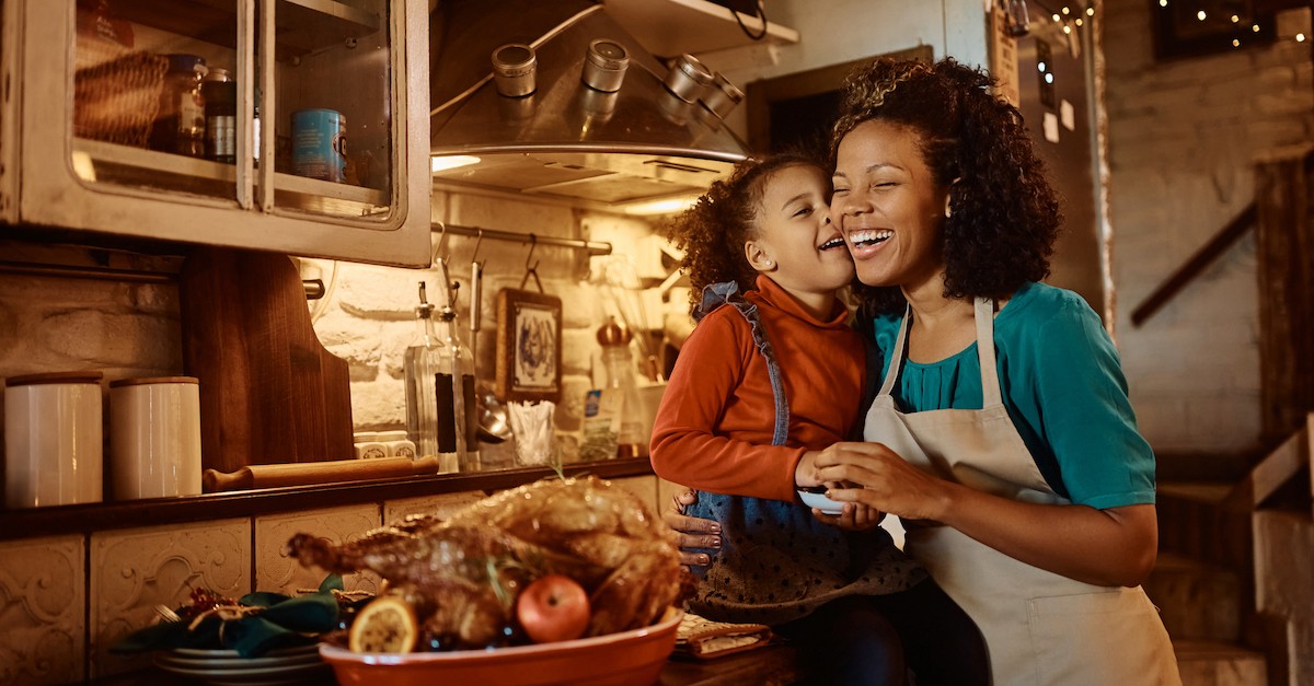 Thanksgiving mom and daughter smiling in kitchen cooking turkey