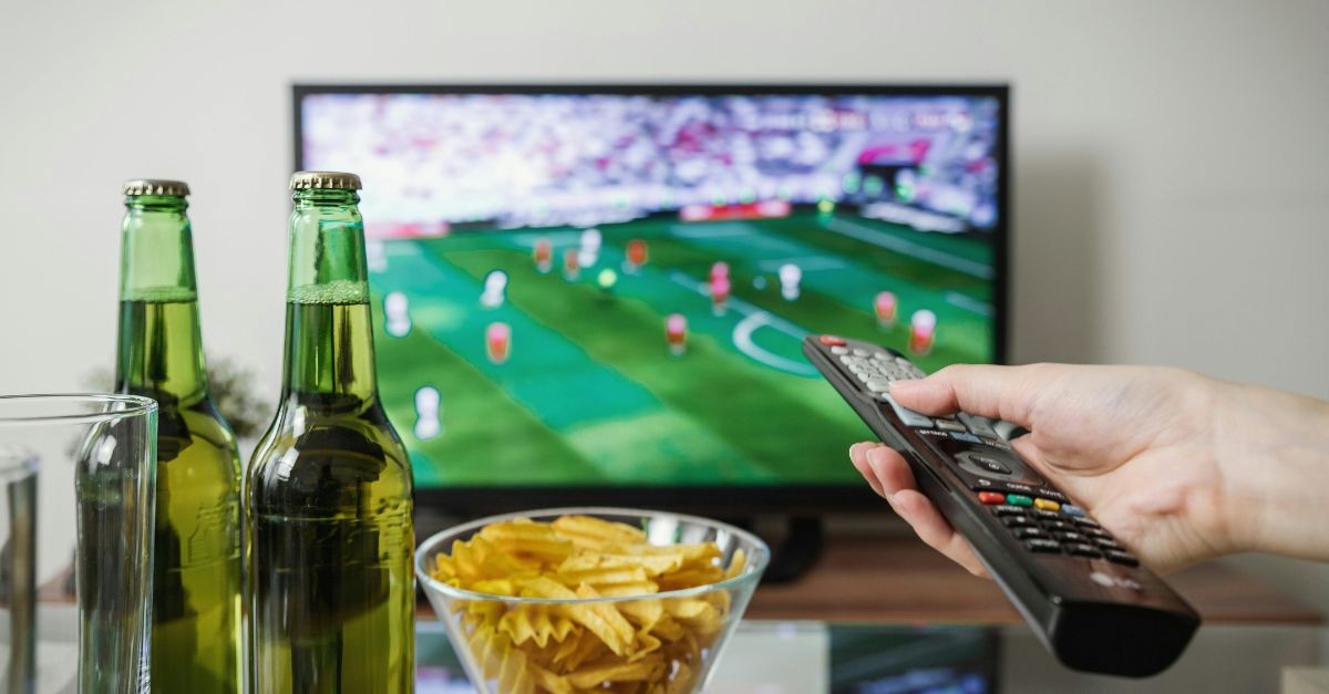 Man pointing remote at the TV, watching football;