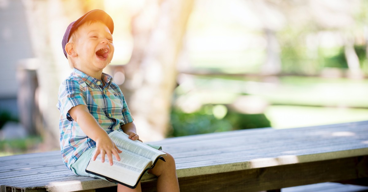 kid smiling reading the bible outside in a hat