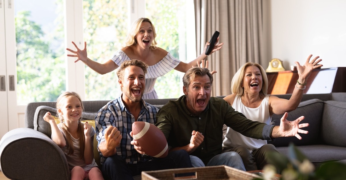 family watching football game excitedly together on sofa; Father's Day