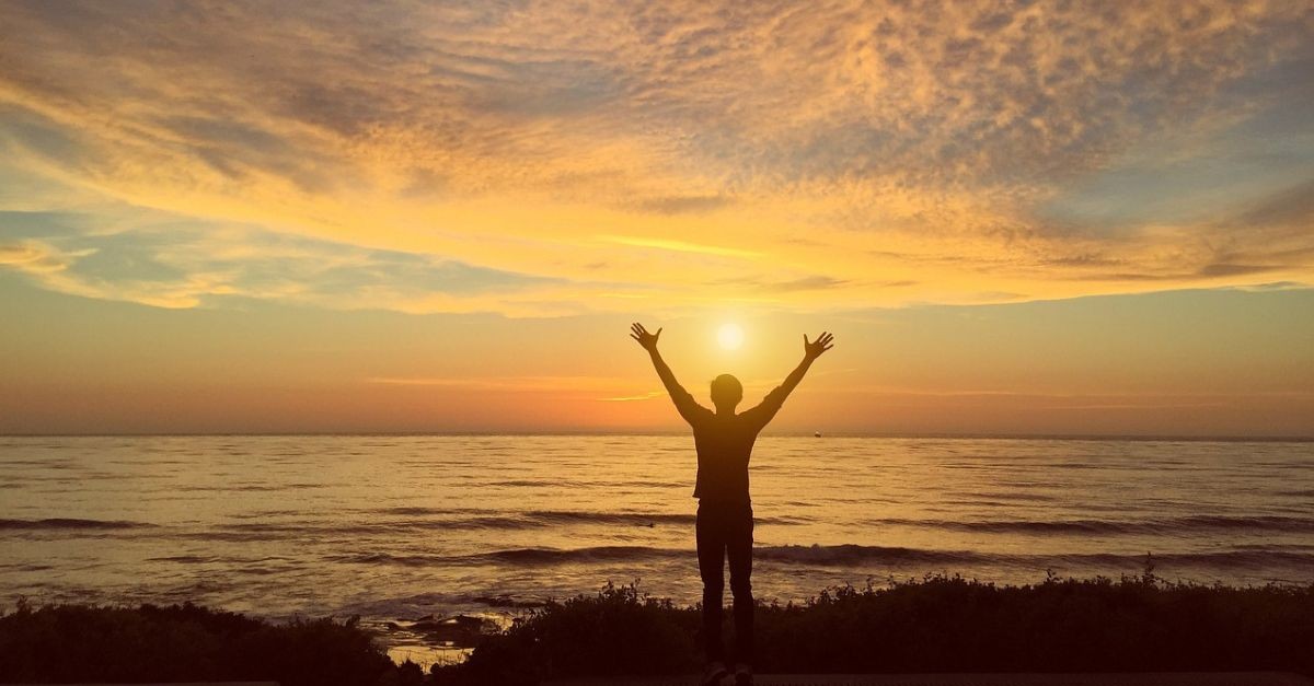 Man with arms raised at sunrise.