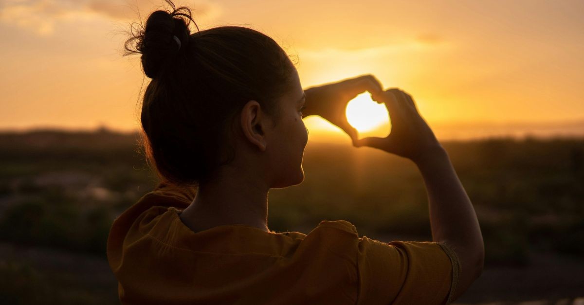 Woman making a heart with her hands at sunrise.
