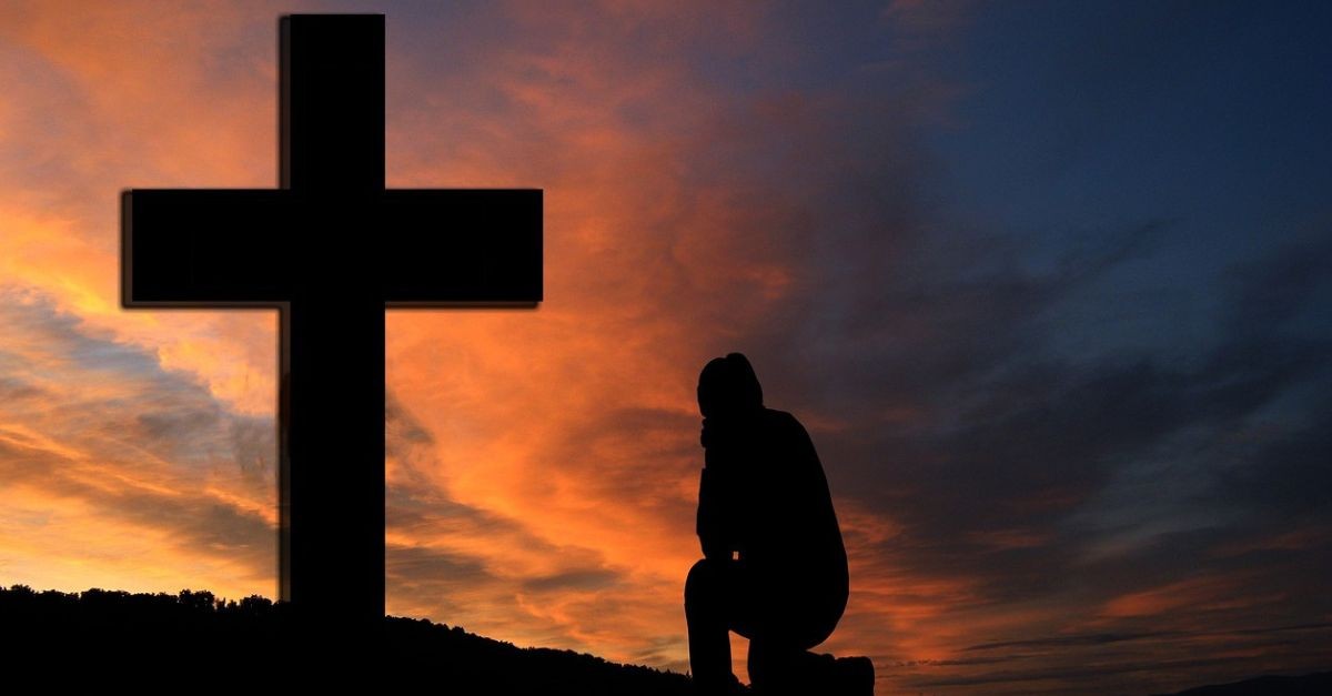 Man praying at the foot of a cross.