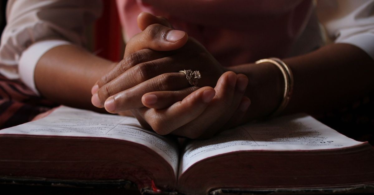 Woman with hands folded in prayer on an open Bible.