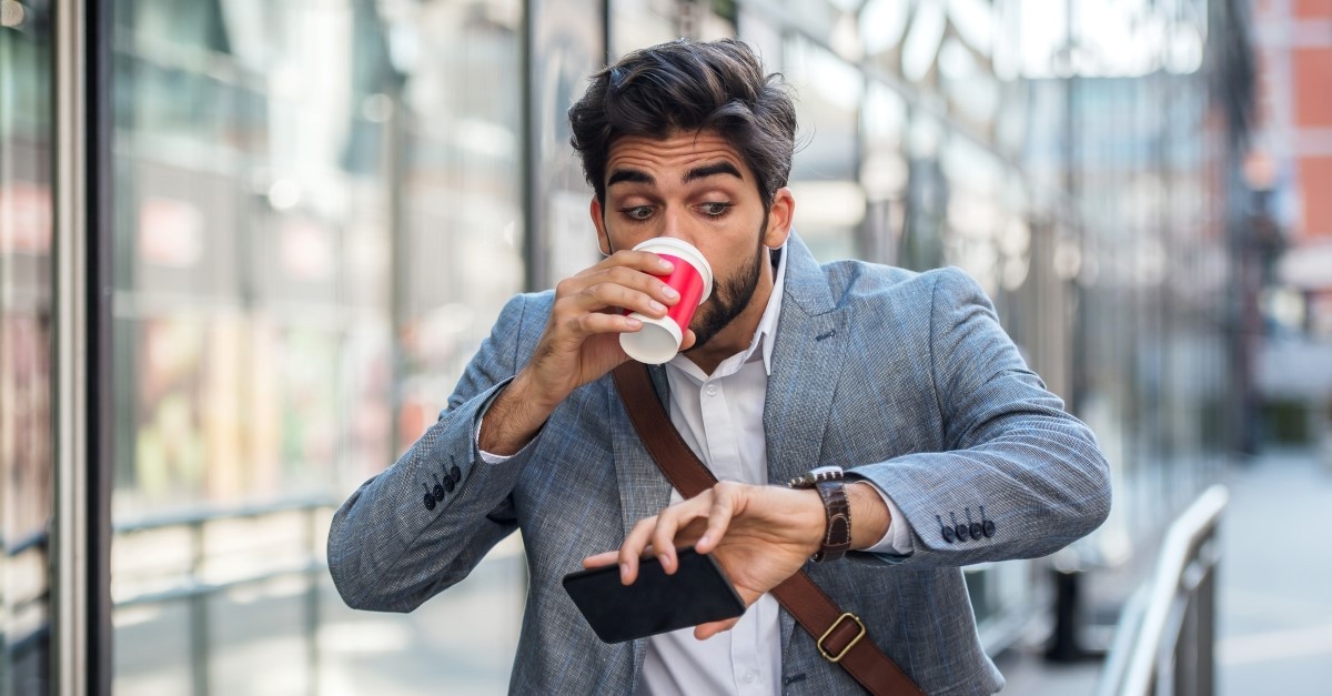 frantic man checking phone and wristwatch while drinking coffee