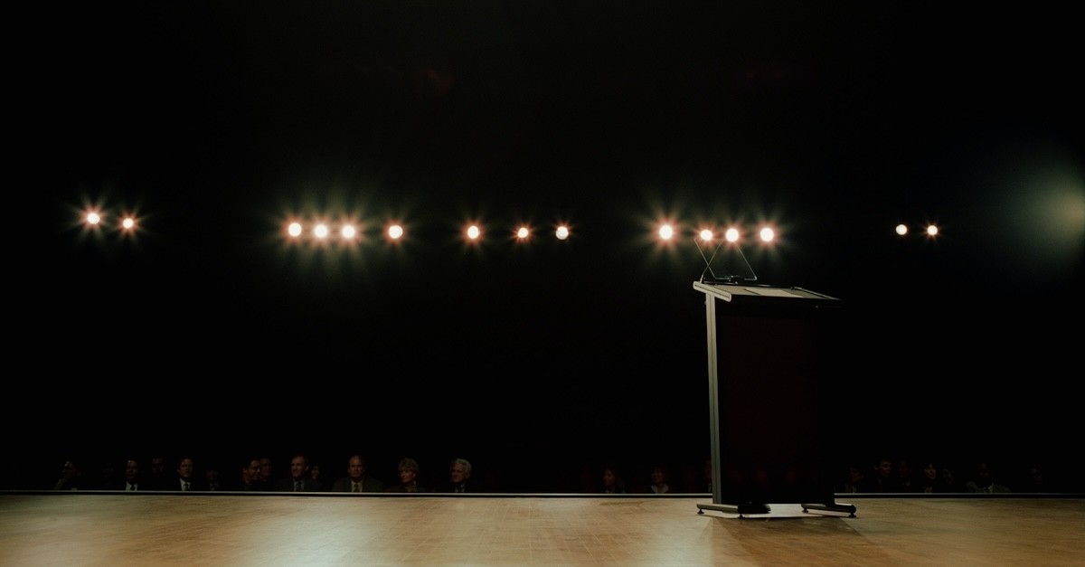 empty stage with bright lights and podium with microphone in front of blacked out audience