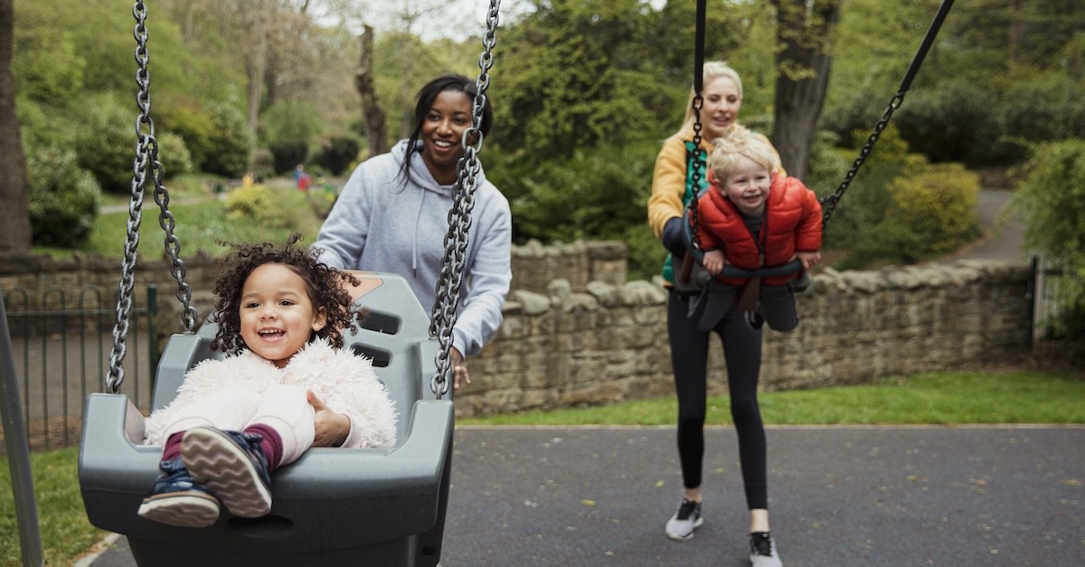 Two moms with kids playing on playground swing set outside