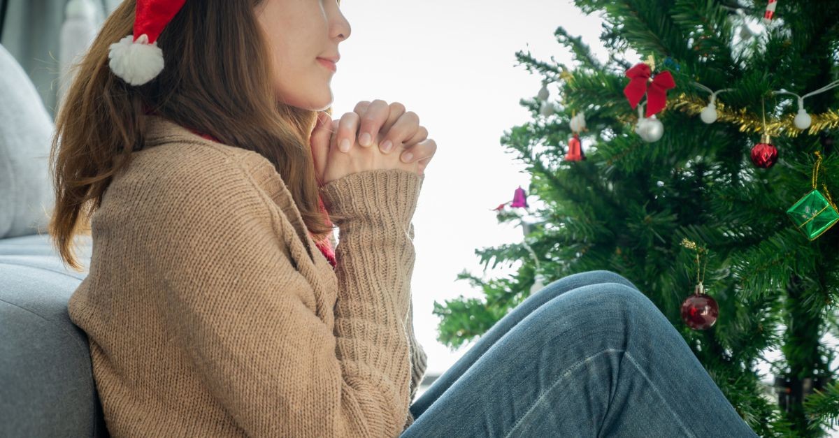 Woman praying by a Christmas tree; prayers for Advent.