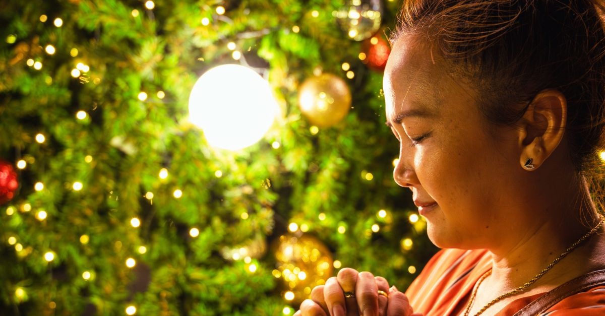 Woman praying by a Christmas tree; prayers for Advent