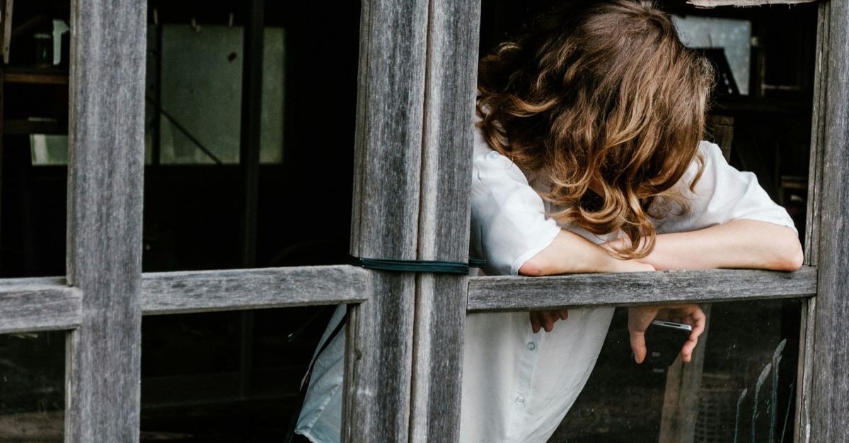 Worried and sad woman by a window; prayers to fight negative emotions.