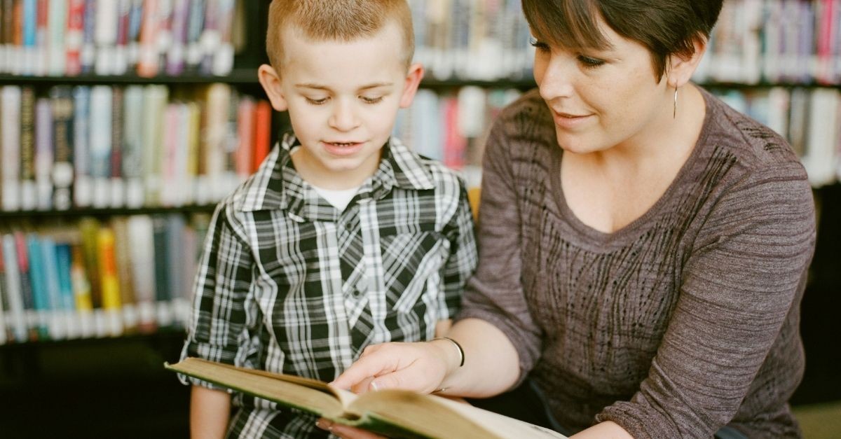 Teacher helping a young student read a book; praying for our kids while they are at school
