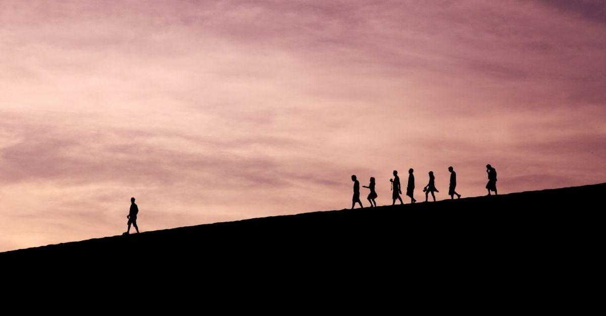 Silhouettes of a group of people walking in a line along a hill at sunset, symbolizing discipleship and following a leader