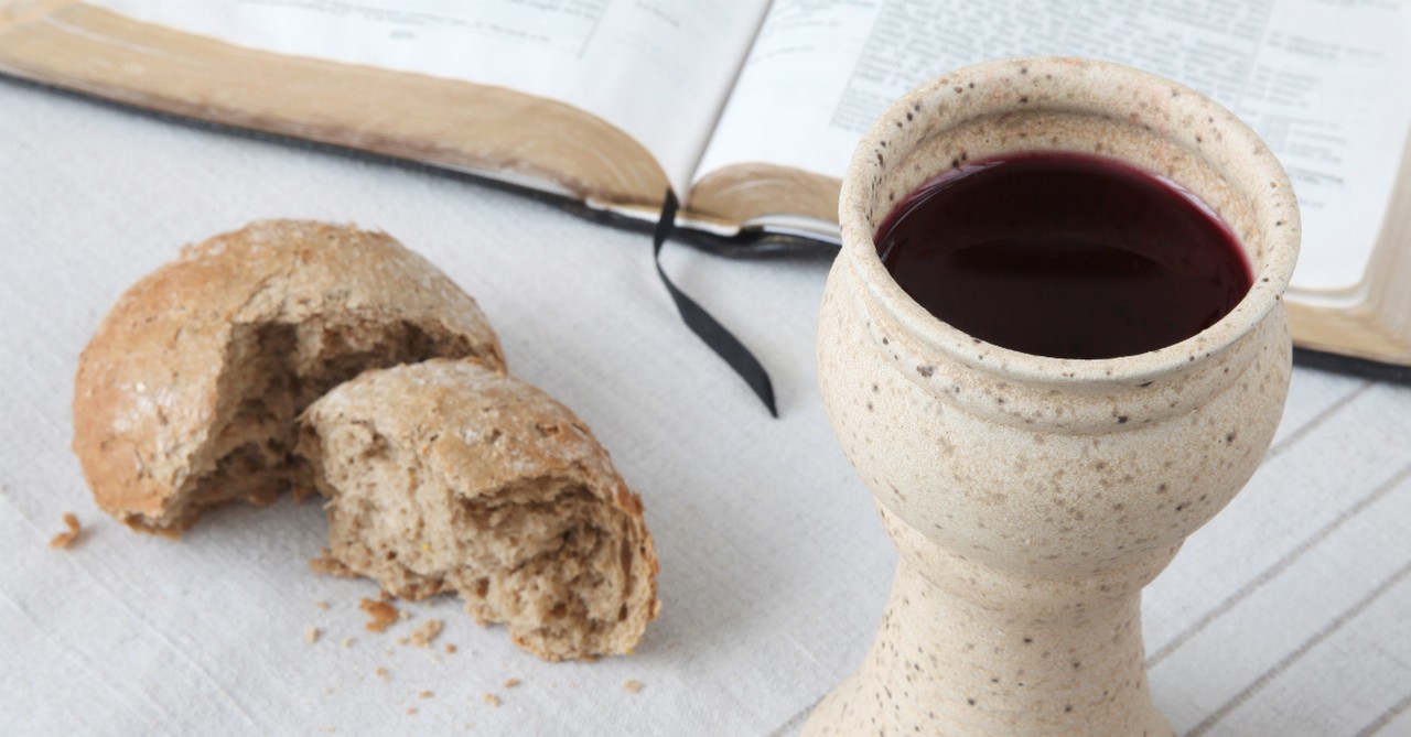 Communion bread and a mug of wine near an open Bible