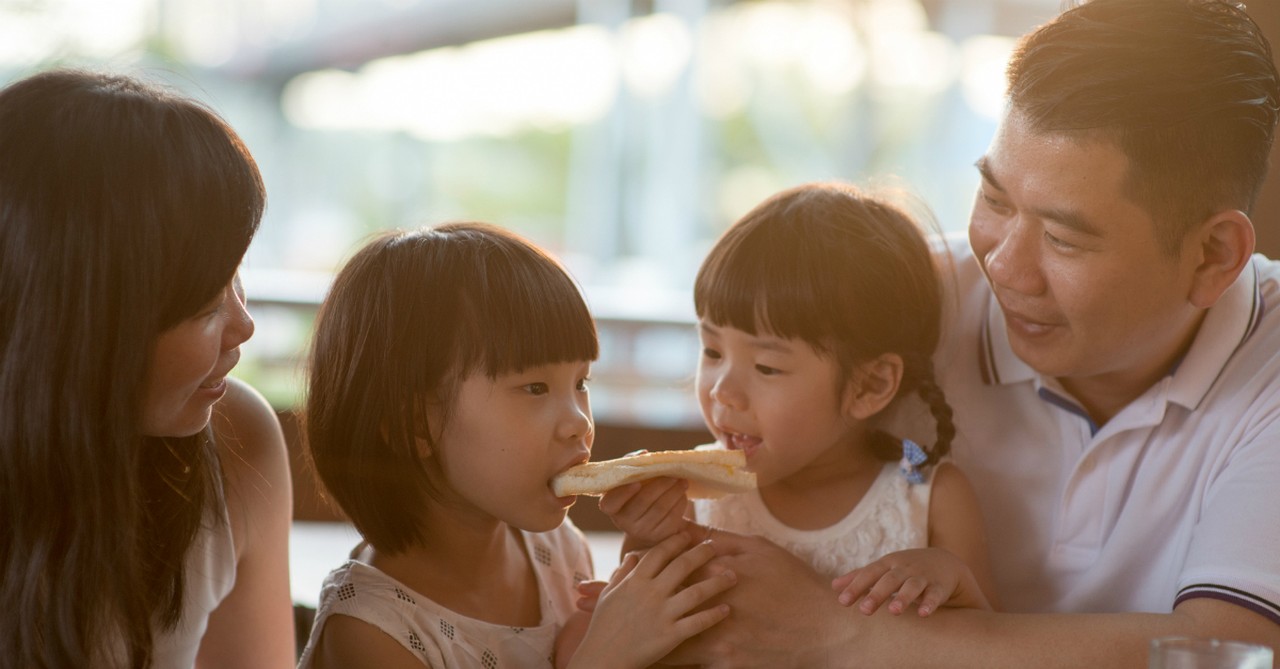 family of four gathered dad is feeding one young daughter toast