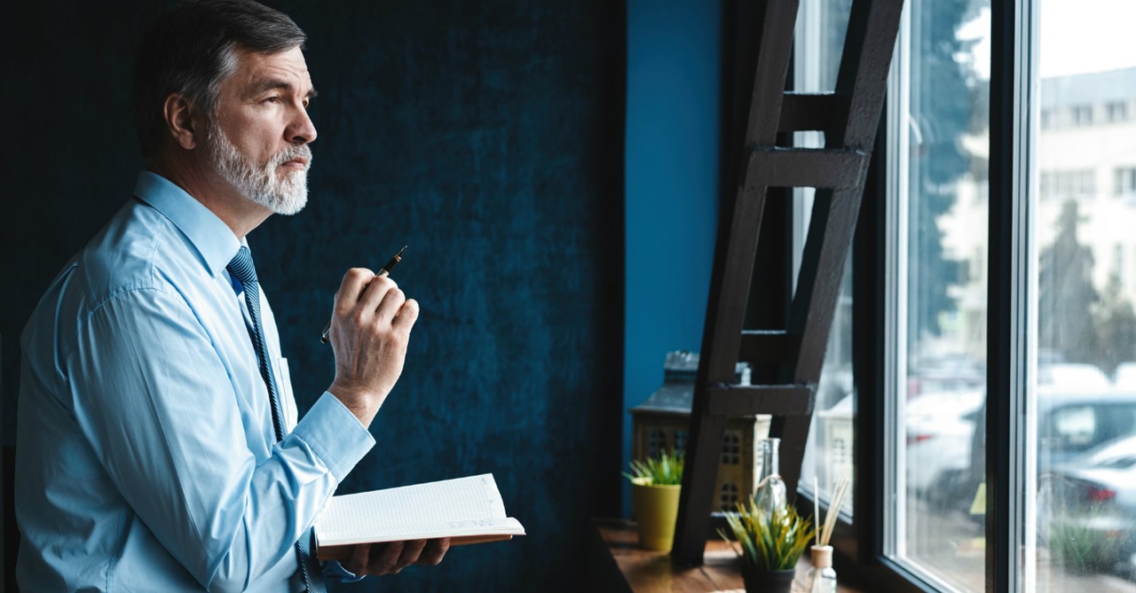 man looking out window in deep thought journaling