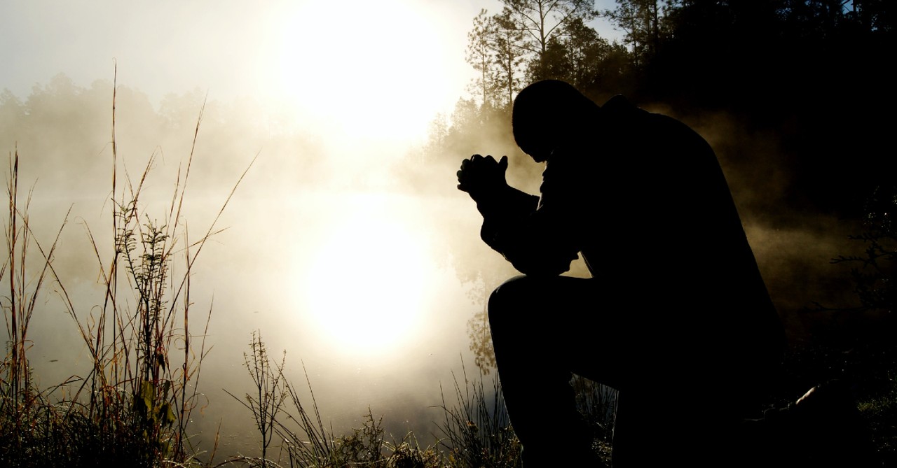 Man kneeling in prayer on a foggy morning