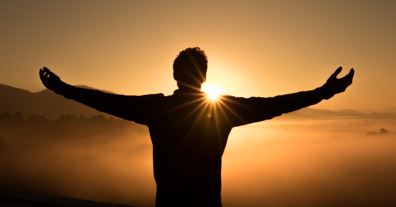 man on mountain at sunset praising