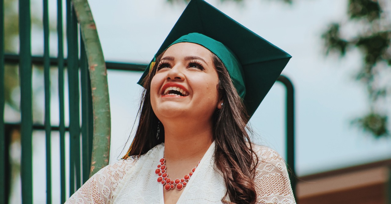 young woman in graduation cap looking up happy