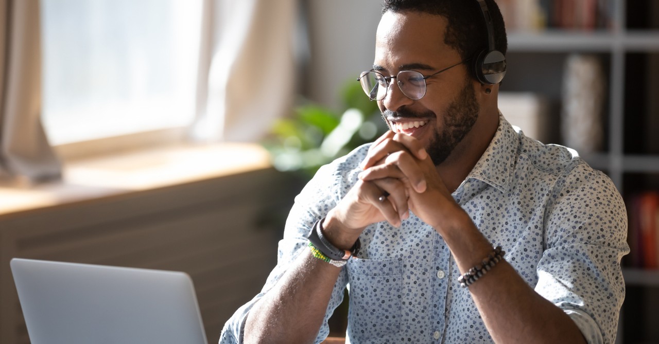 man with headphones smiling with joy into laptop watching video