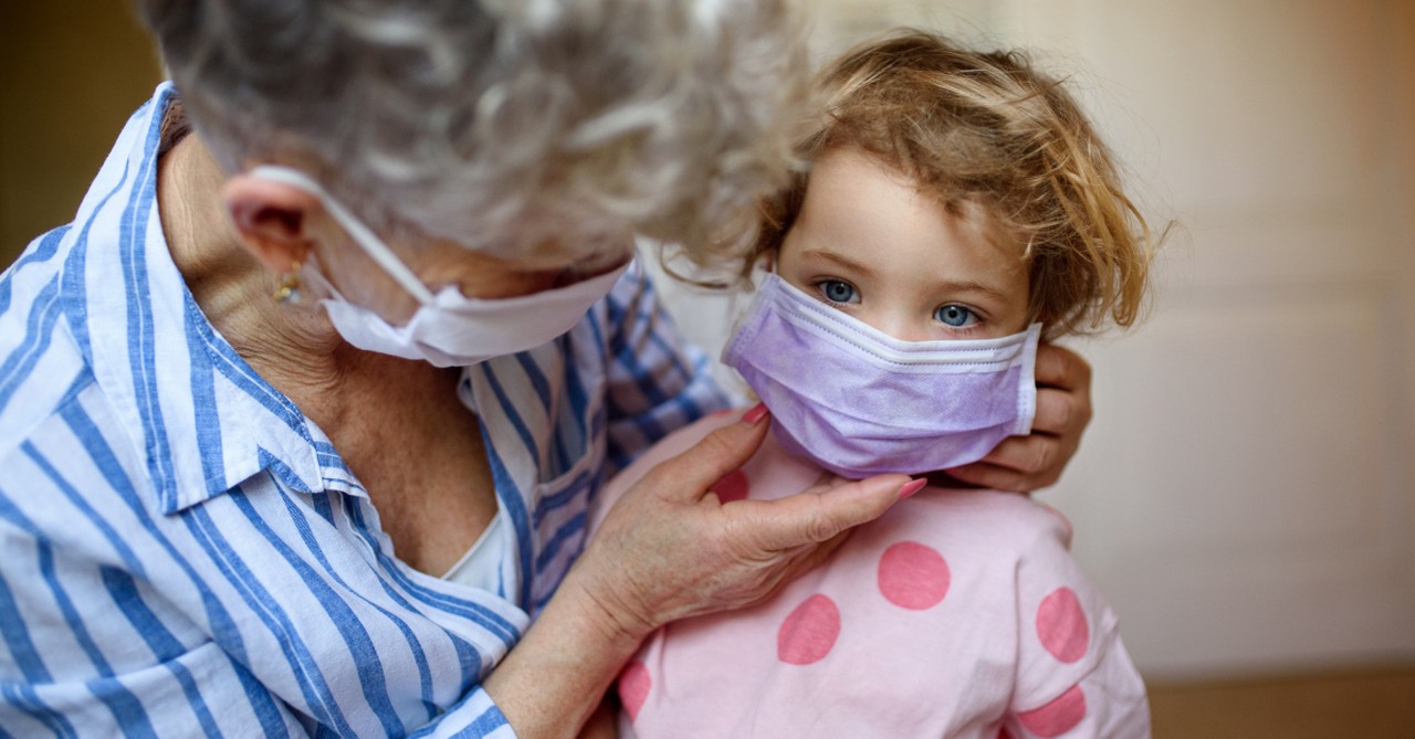 senior woman grandmother putting face mask on granddaughter coronavirus