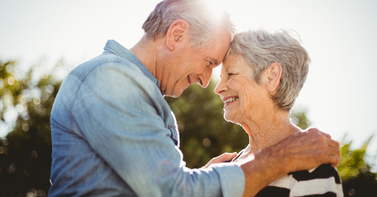 senior adults facing each other hug at sunset happy