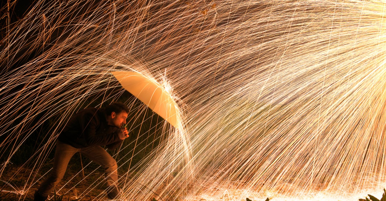 man protecting self from fire sparks with umbrella