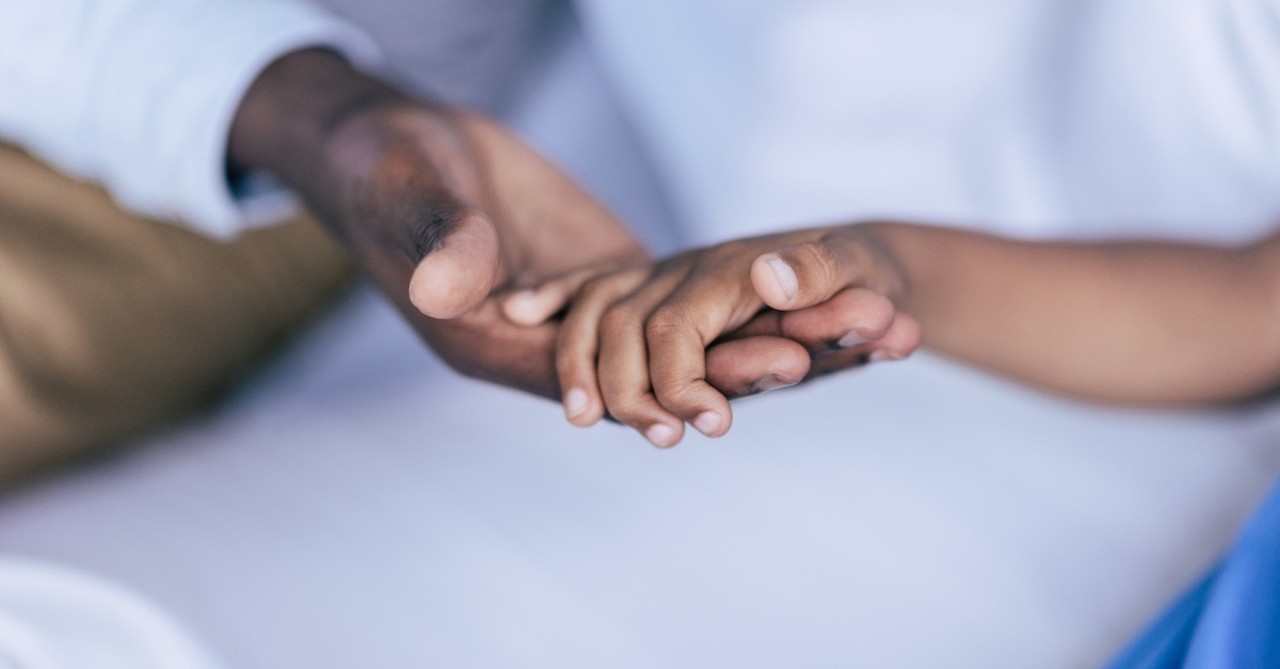 father holding child's hand from bed