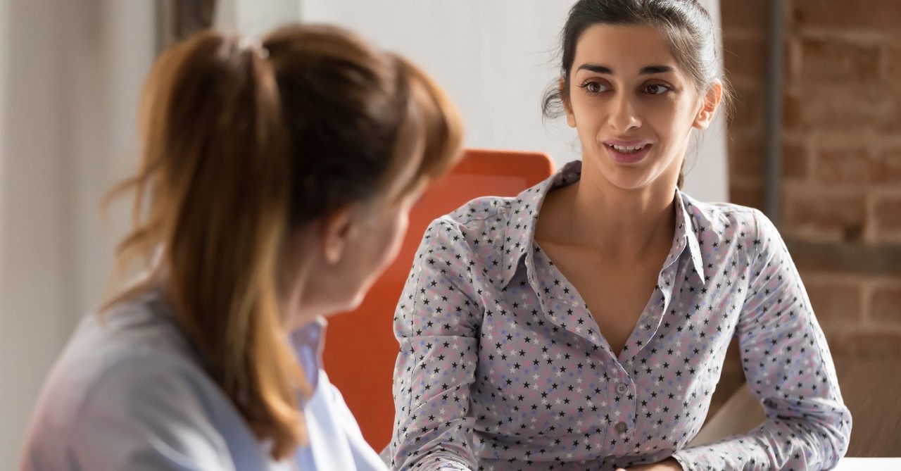 two women in business clothes talking at a desk