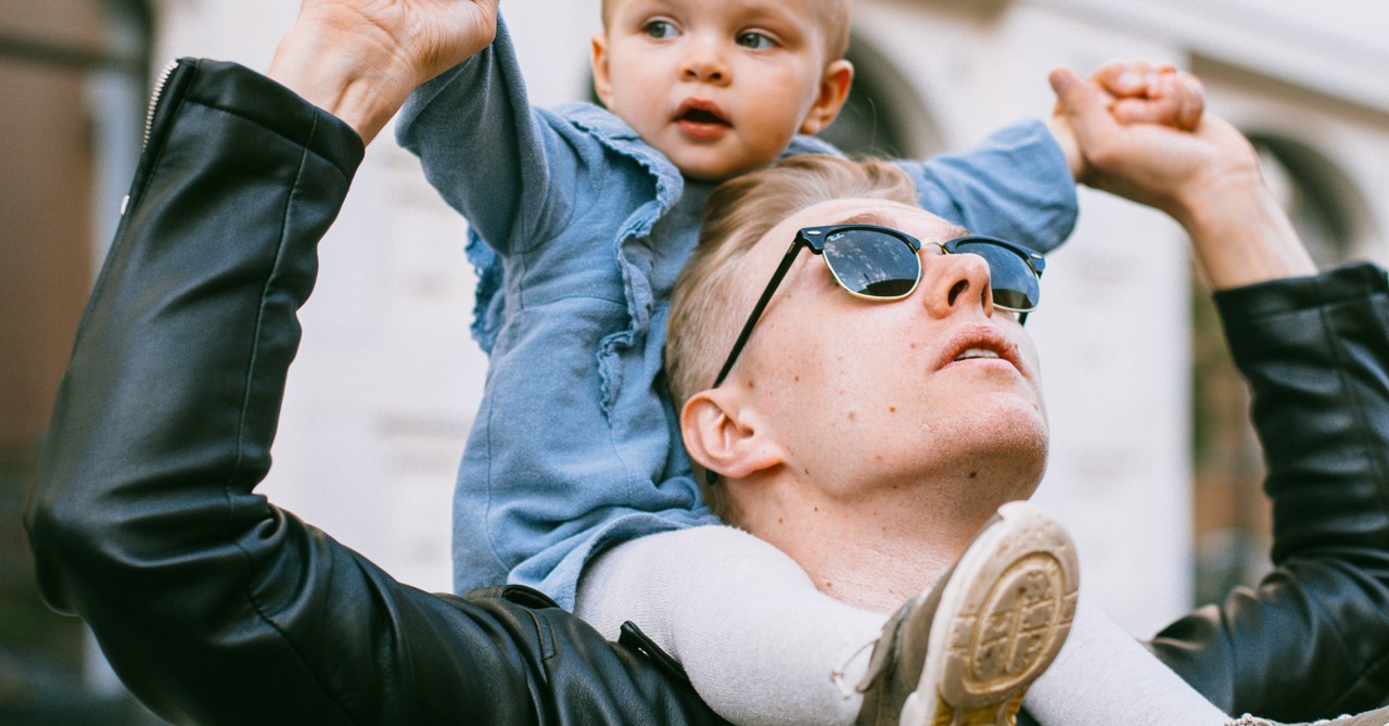 young father with baby daughter on shoulders looking up