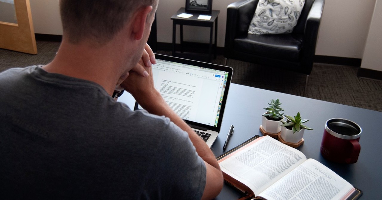 A man contemplates his computer screen and his Bible together