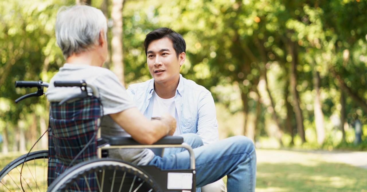 man kneeling down to have conversation with senior in wheelchair