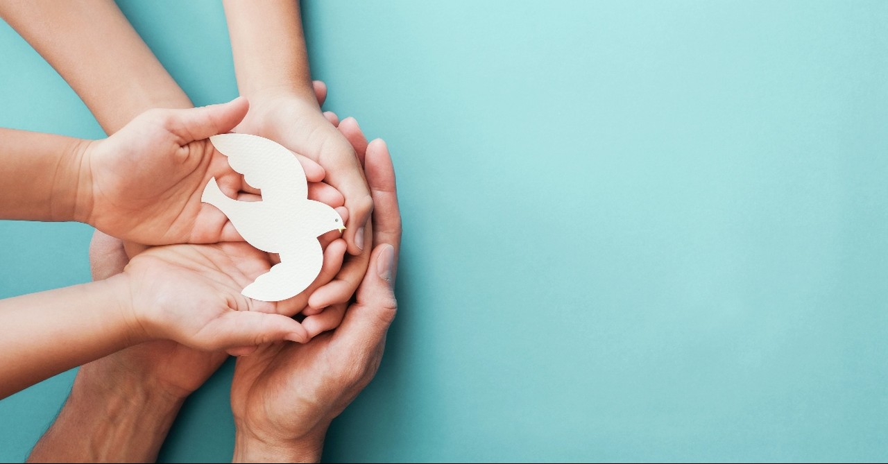 Three hands holding a paper dove