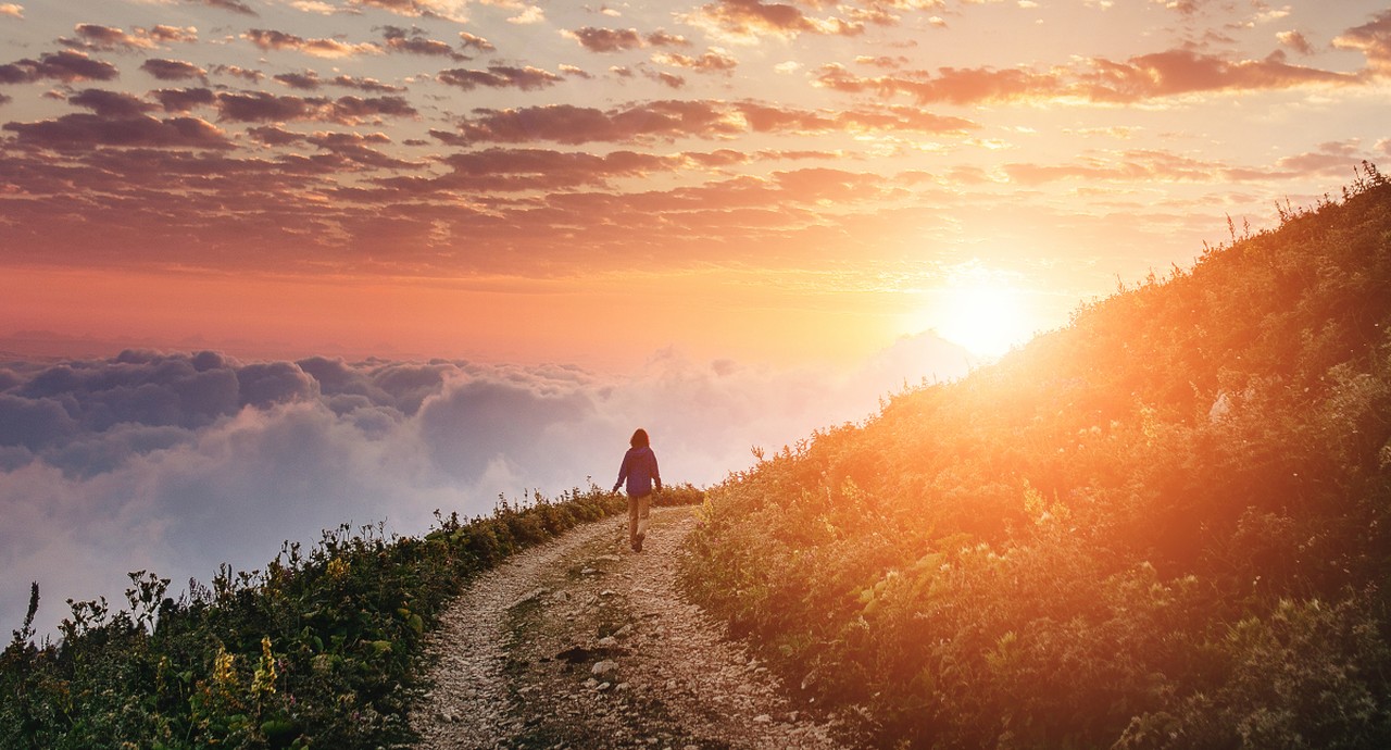 woman hiking on trail around mountian toward sunset