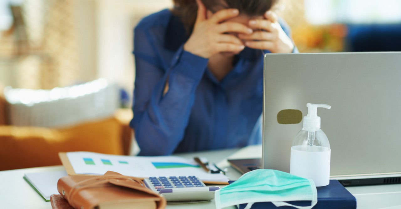 woman stressed at work desk with face mask sanitizer wallet laptop