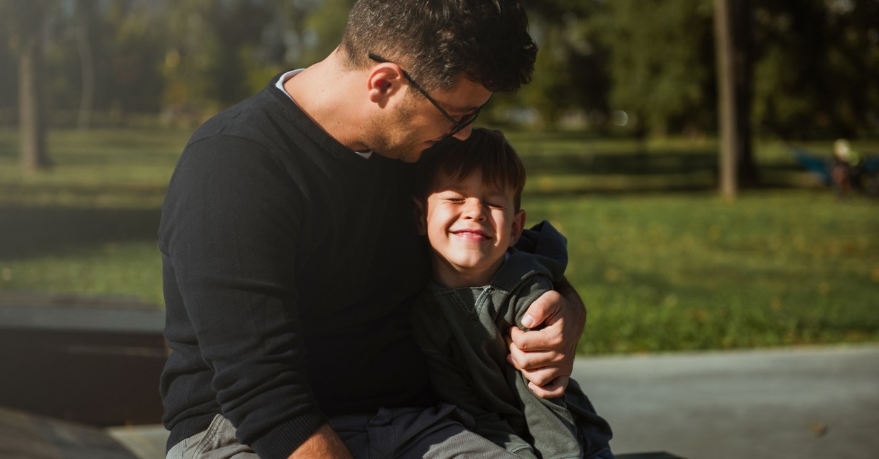 father and son sitting on ramp in park hugging and smiling