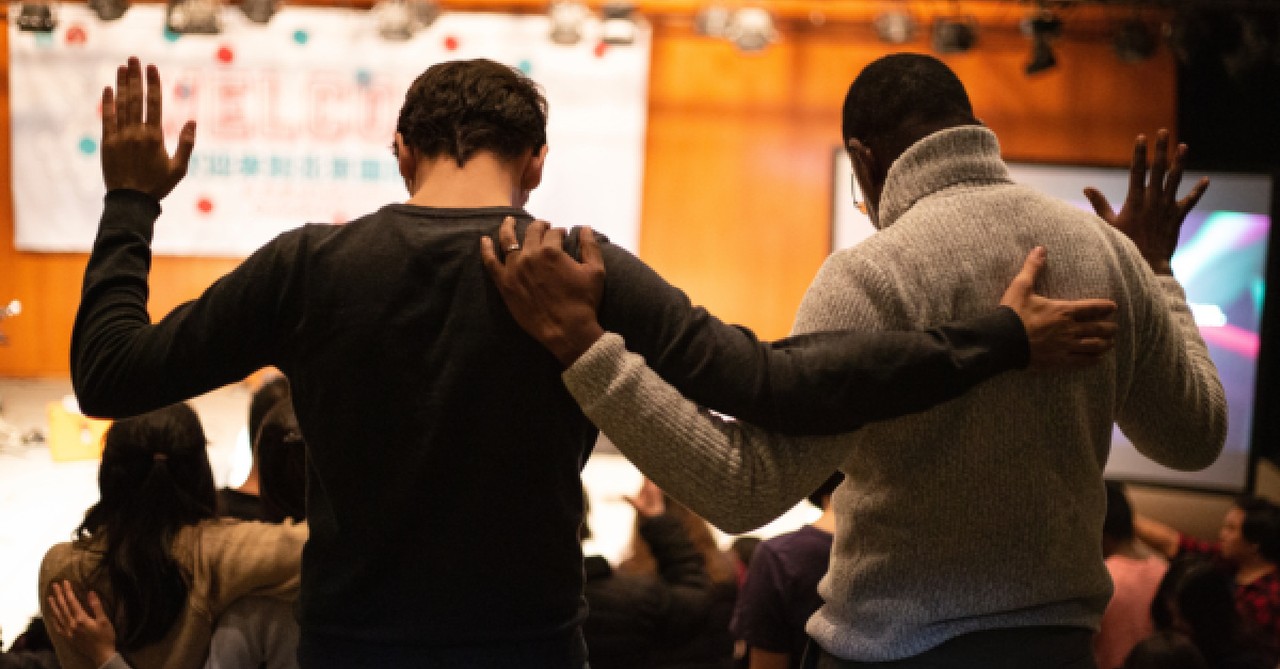 Two men with arms around each other, and a hand raised in prayer