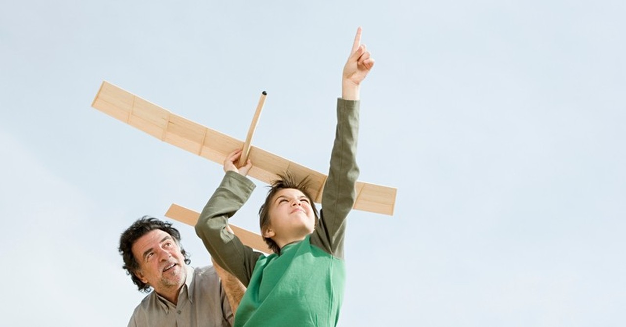 grandson and grandfather playing and pointing up to launch balsa wood airplane