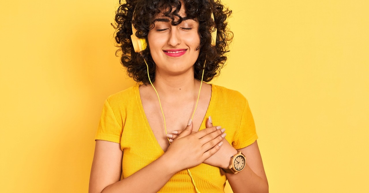 woman on yellow background listening to worship music with headphones hand over heart