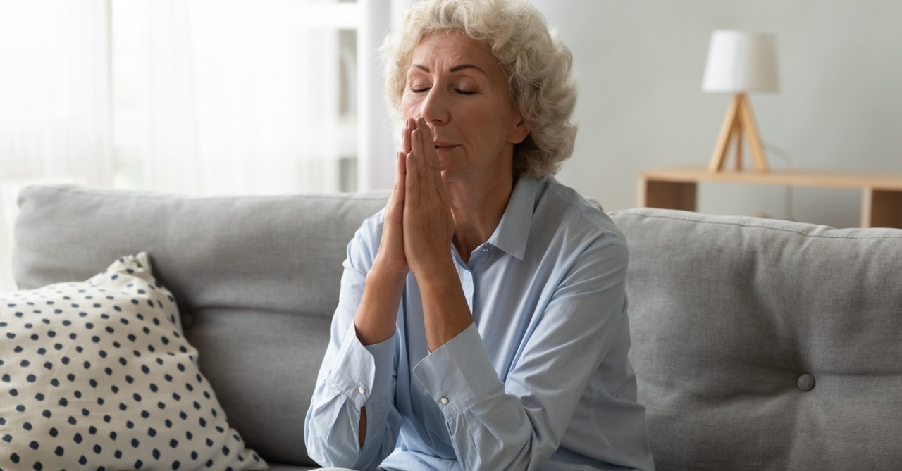 senior woman on couch eyes closed in thoughtful prayer