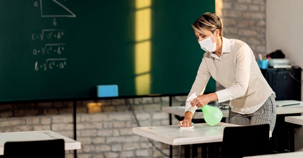 teacher wiping down desks cleaning in classroom wearing mask, challenges teachers facing covid