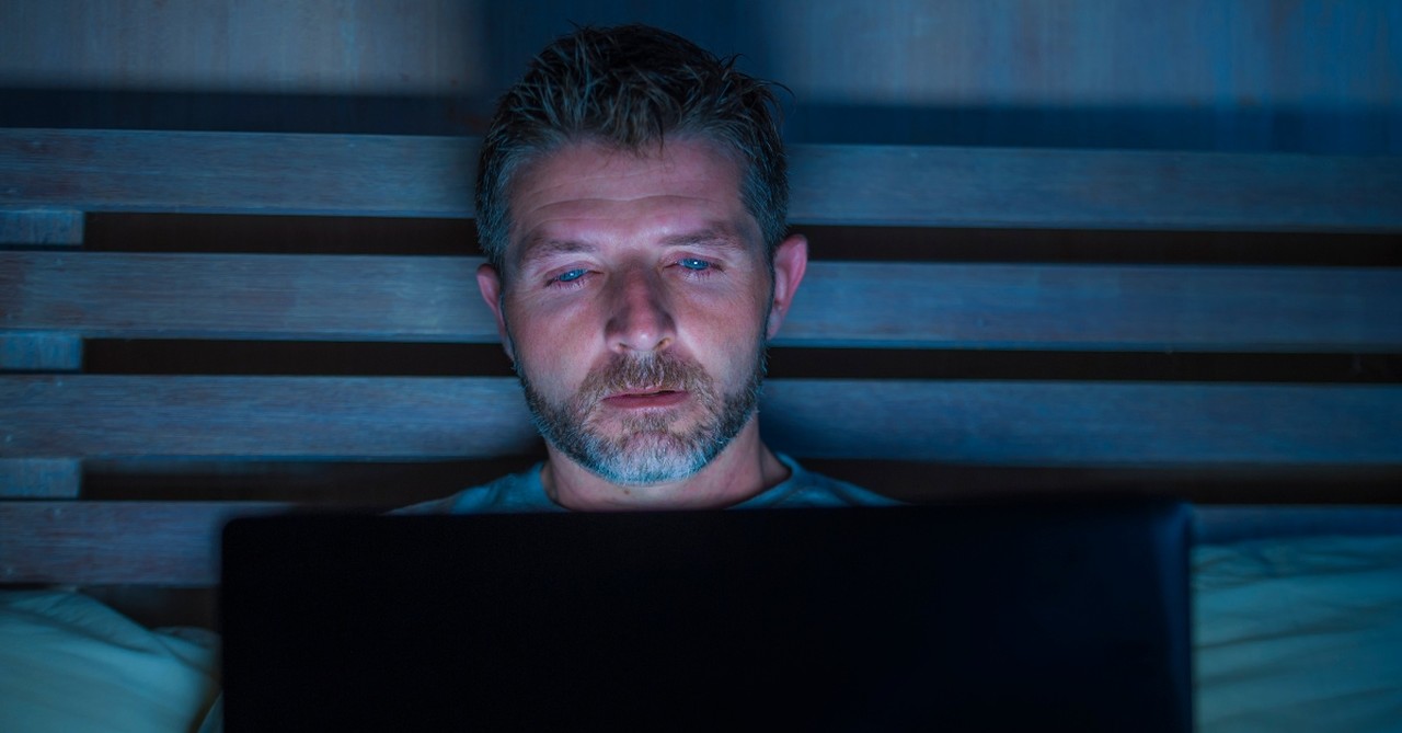 man watching laptop late at night in bed