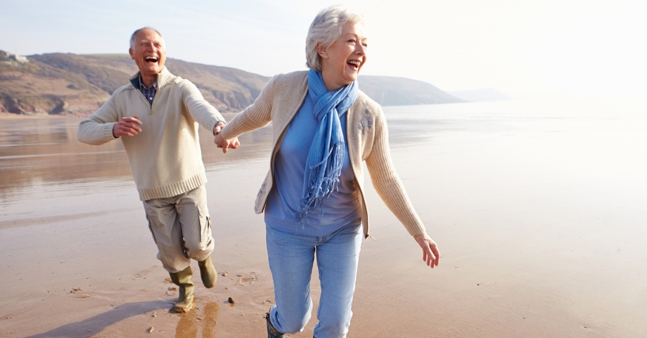 happy senior couple running along beach